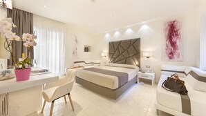 A modern hotel room with a large bed, a desk with a chair, a bedside table, and a large window with curtains. - Palazzo Montefusco Relais (Sorrento)