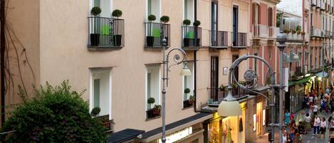 A multi-story building with balconies, storefronts, and a street with pedestrians.
