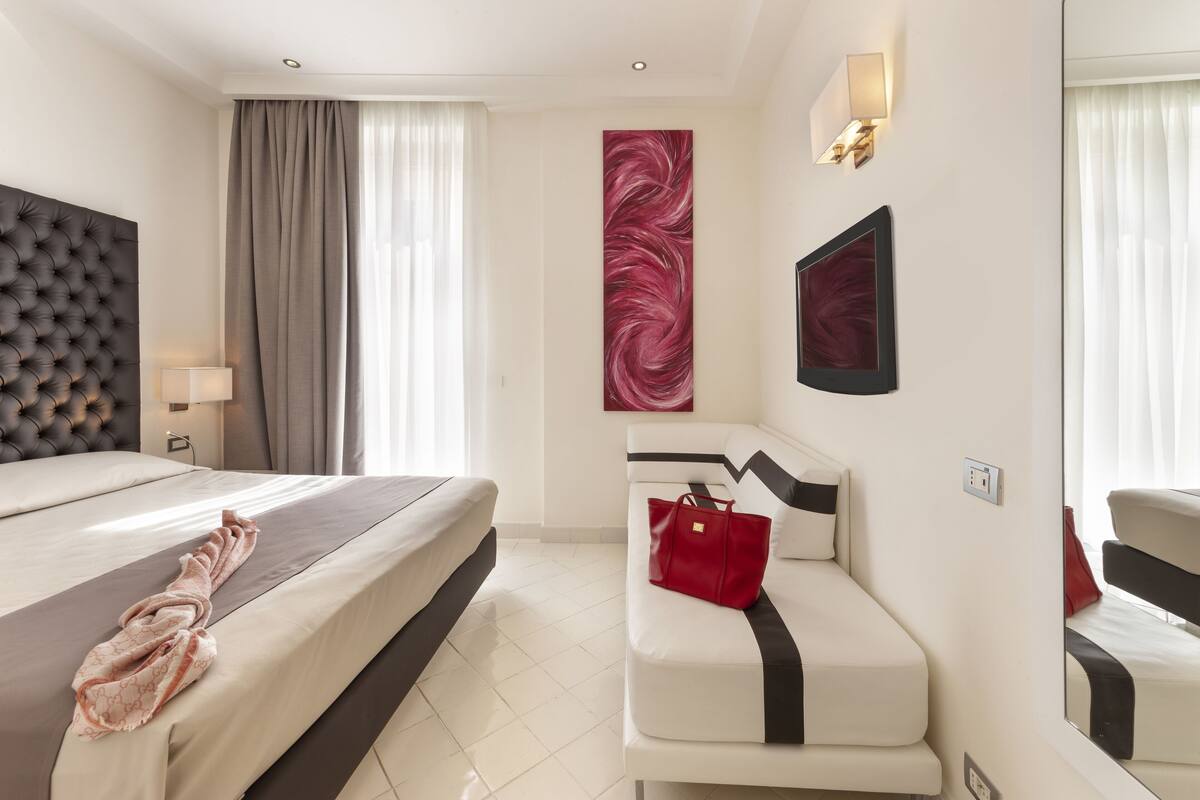 Ein Hotelzimmer mit einem großen Bett, einer Couch, einer roten Handtasche und einem Wandbild.