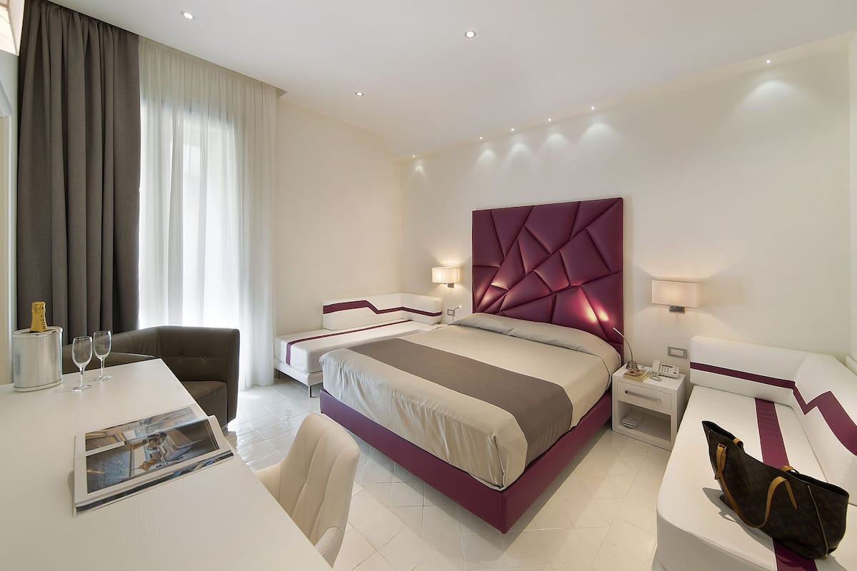 Ein modernes Hotelzimmer mit einem großen Bett, zwei Nachttischen, einem Schreibtisch, einem Stuhl und einem großen Fenster mit Vorhängen.