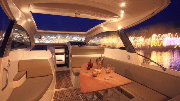 A yacht interior with a dining area, cushioned seating, and a view of a cityscape at night. - Palazzo Montefusco Relais (Sorrento)