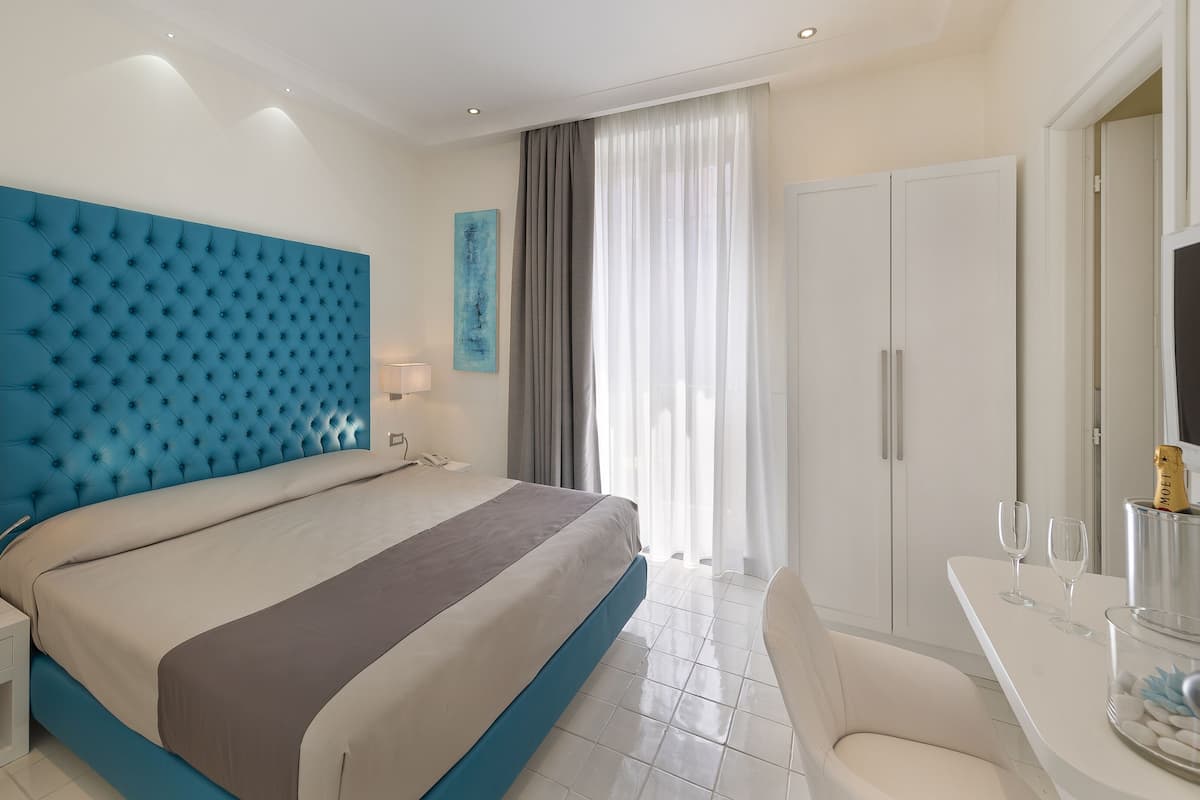 Ein modernes Hotelzimmer mit einem großen Bett, einem Nachttisch, einem Schreibtisch mit Stuhl und einer Minibar.