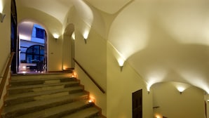A staircase with warm lighting, a wooden handrail, and a view into a room with a balcony. - Palazzo Montefusco Relais (Sorrento)