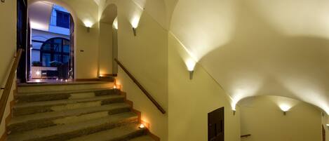 A staircase with warm lighting, a wooden handrail, and a view into a room with a balcony.
