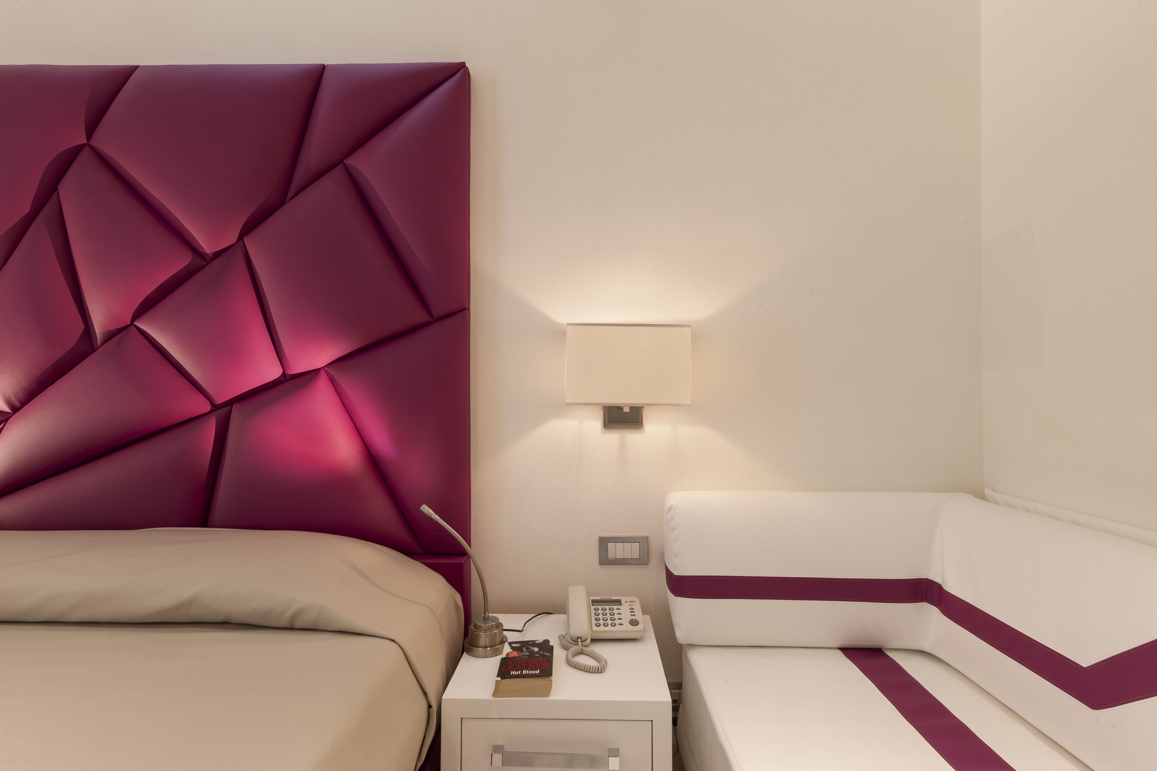 Une chambre d’hôtel au design moderne, comprenant un grand lit avec une tête de lit, une table de chevet avec une lampe, un téléphone et un petit coffre-fort.