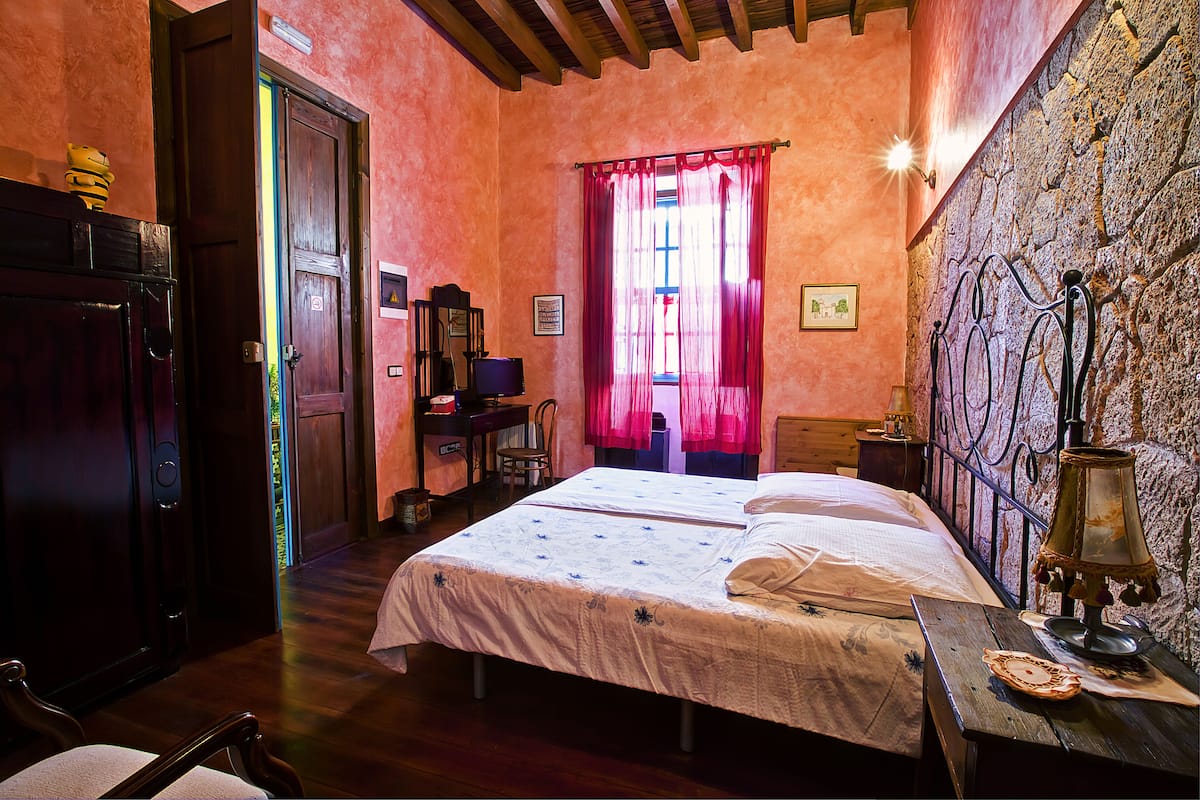 Una habitación con una cama, muebles de madera, un escritorio y una pared de piedra.