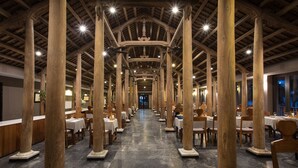 A long corridor with high wooden beams and evenly spaced columns, leading to a dining area with tables and chairs. - Vedana Lagoon Resort and Spa (Hue)