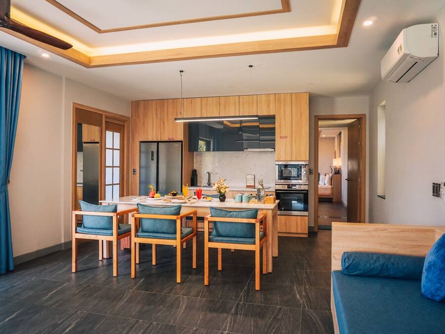 A modern kitchen with wooden cabinets, a dining area with blue chairs, and a sofa.