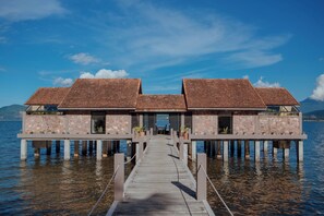A wooden pier leading to a row of overwater bungalows with stone walls and thatched roofs. - Vedana Lagoon Resort and Spa (Hue)