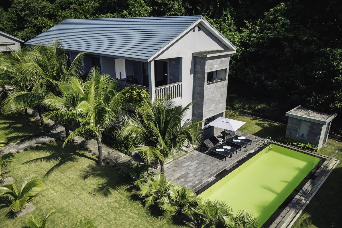 Ein modernes Haus mit Swimmingpool, umgeben von Palmen und einem gepflegten Rasen.
