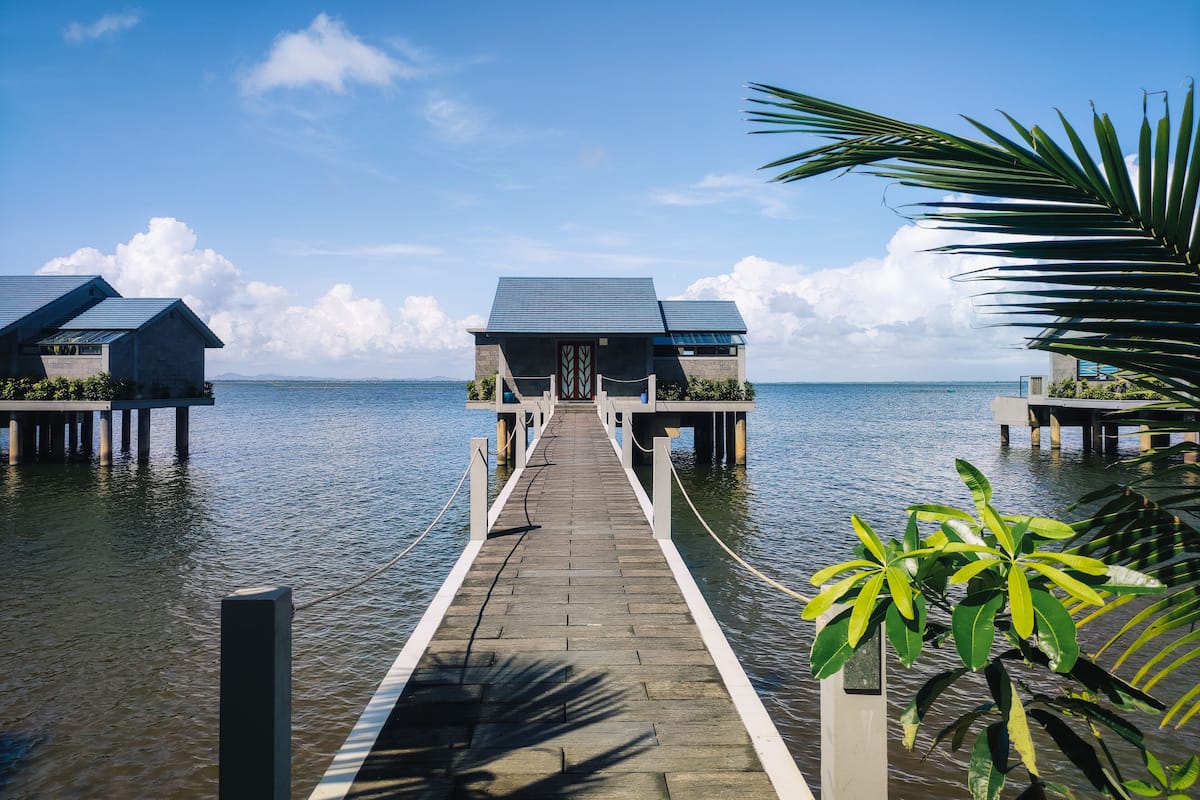 Eine Holzstege führt zu Bungalows über dem Wasser, mit freiem Blick auf das Meer.