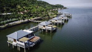 Overwater bungalows with a view of the sea and a forested hillside. - Vedana Lagoon Resort and Spa (Hue)