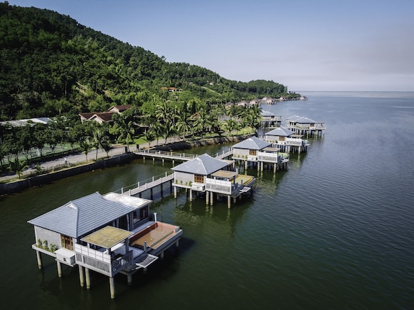 Bungalows auf Stelzen mit Blick auf das Meer und einen bewaldeten Hügel.