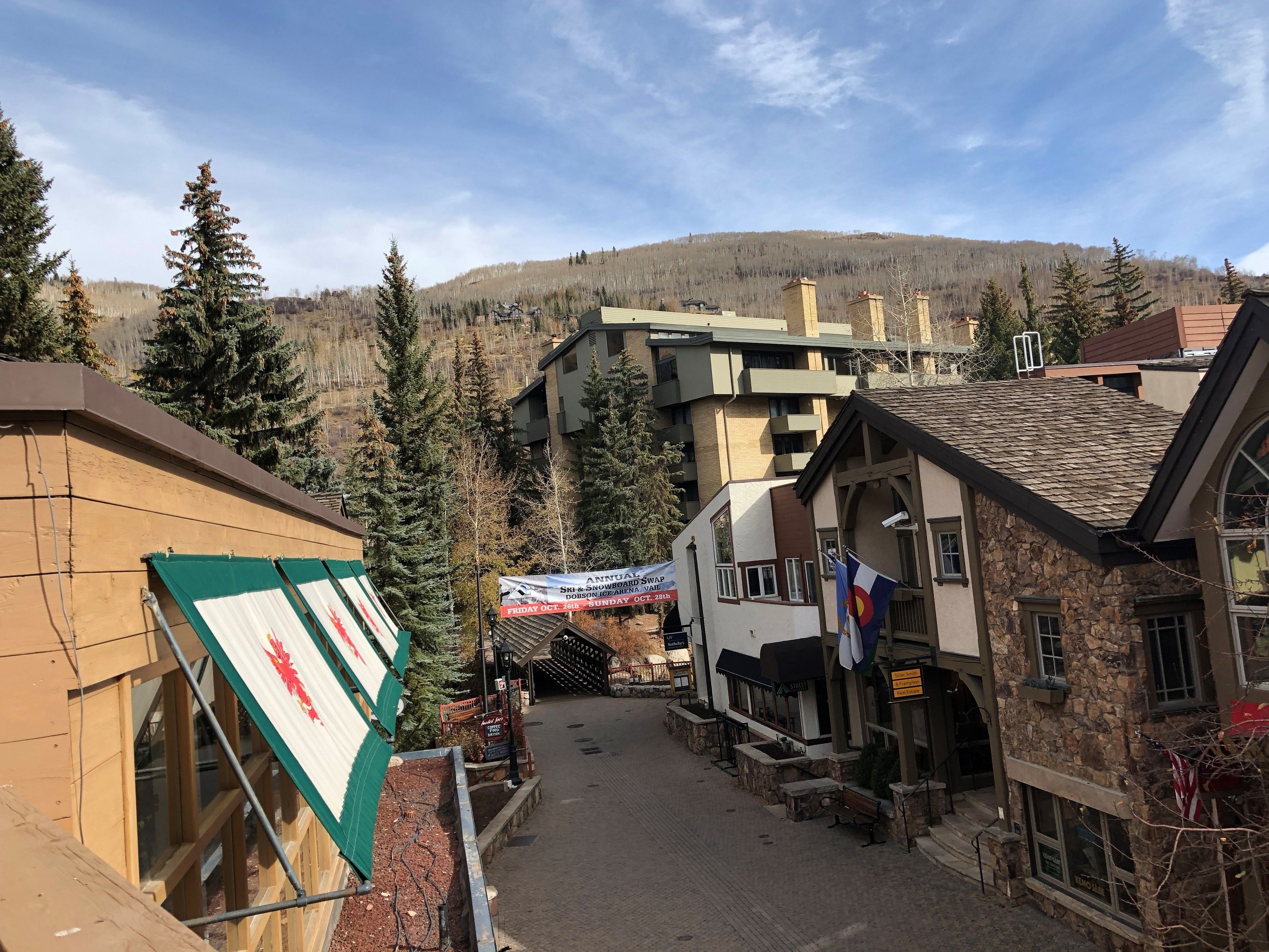 Une place de ville avec des bâtiments, une pancarte annonçant un événement annuel d’échange de matériel de ski et de raquettes, et une montagne en arrière-plan.