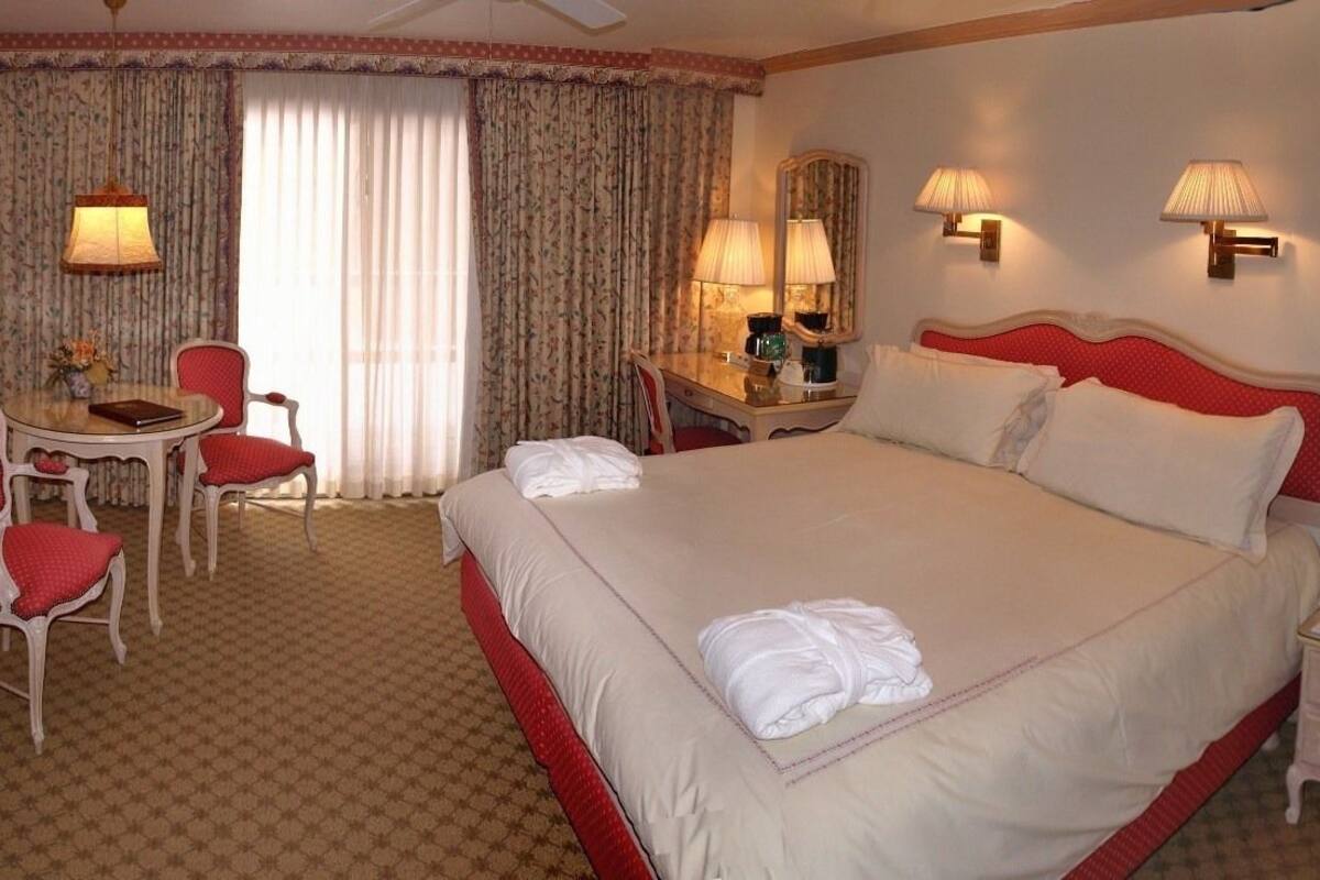 Een hotelkamer met een groot bed, een bureau met stoel, een klein tafeltje en twee lampen.