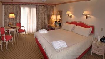 A hotel room with a large bed, a desk with a chair, a small table, and two lamps.