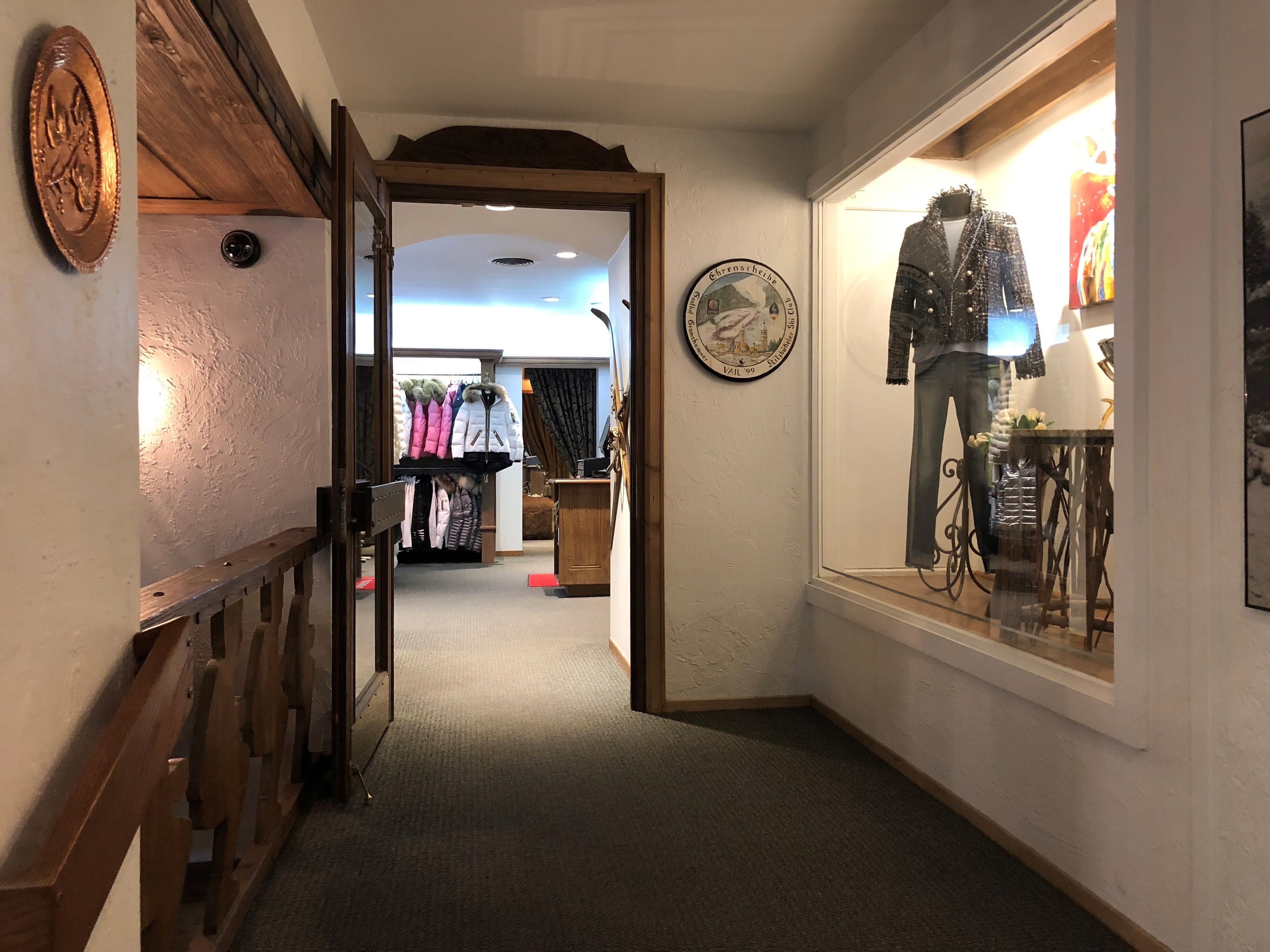 A corridor with a wooden railing, a clothing rack, and a mannequin in a window display.