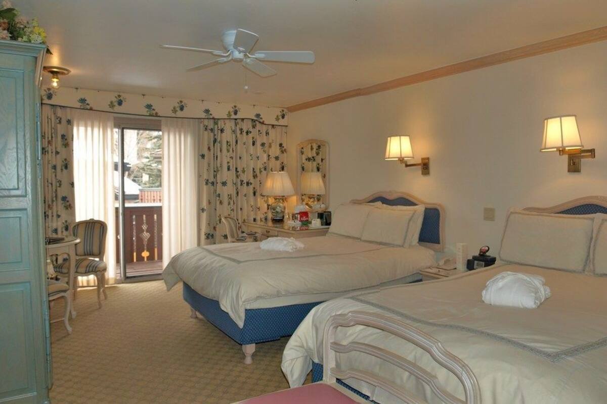 Hotelkamer met twee bedden, een plafondventilator, een balkon met gordijnen en twee wandlampen.