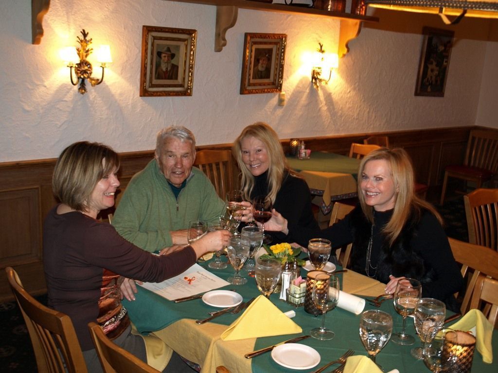 Un grupo de personas sentadas alrededor de una mesa en un comedor con sillas de madera y mantel verde.