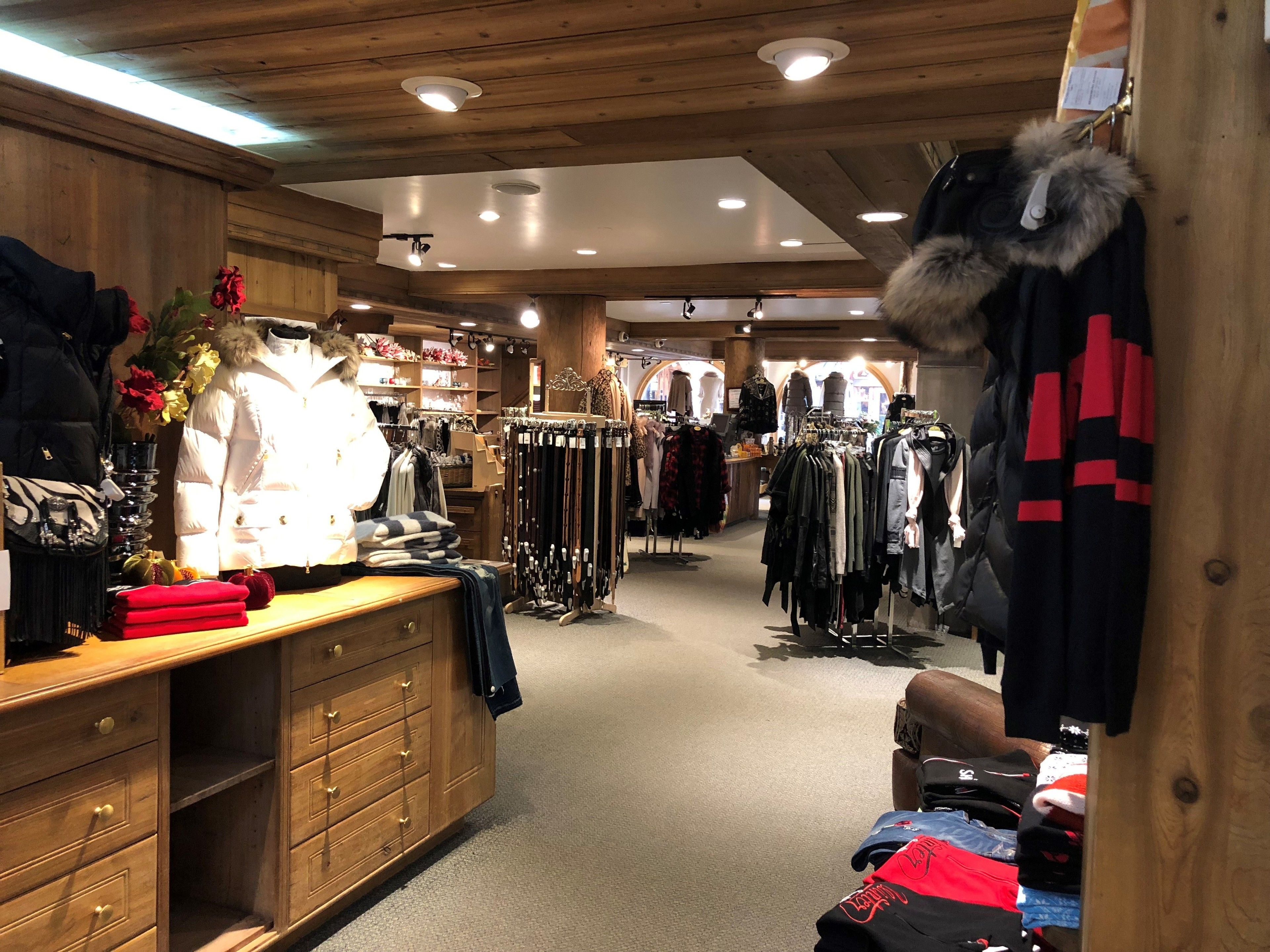 A clothing store with wooden interiors, racks of clothes, and a mannequin.