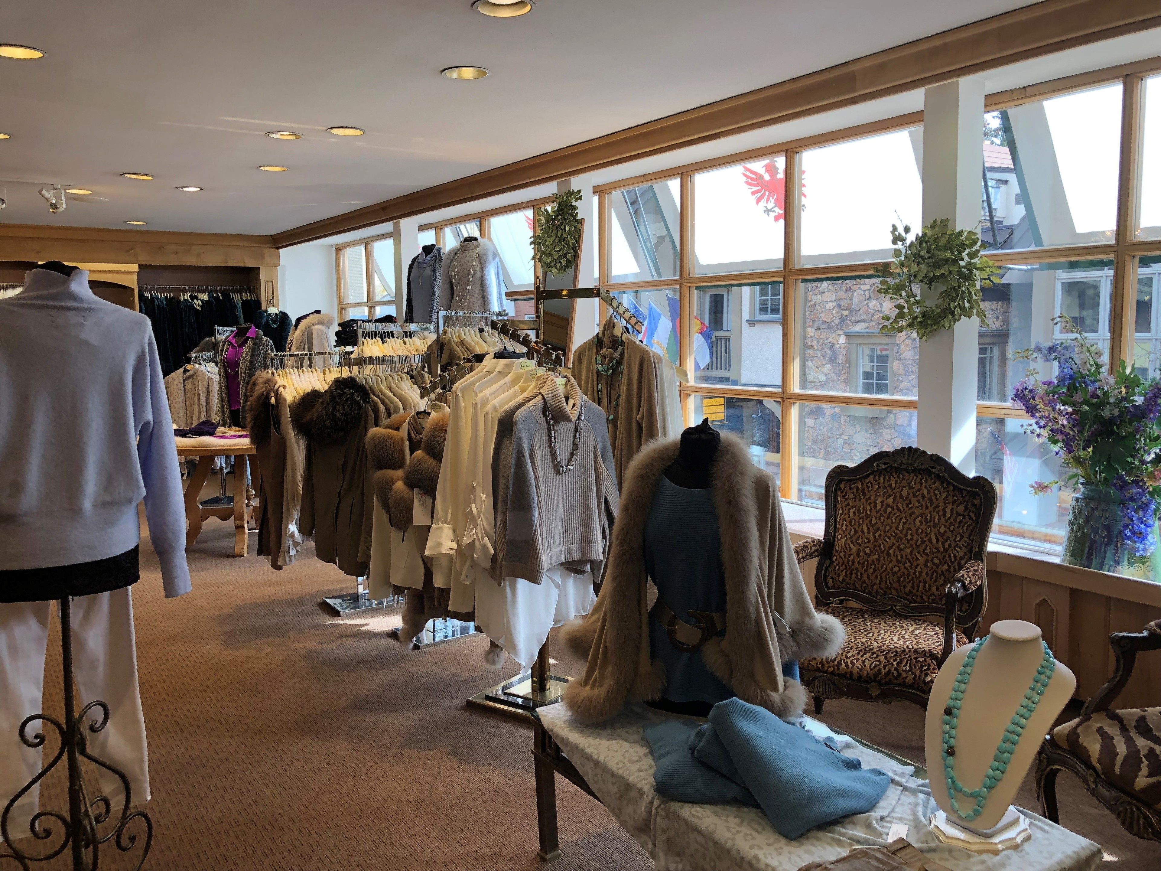 Un magasin de vêtements avec des portants remplis de vêtements, des mannequins et une table de présentation où sont exposés divers articles.