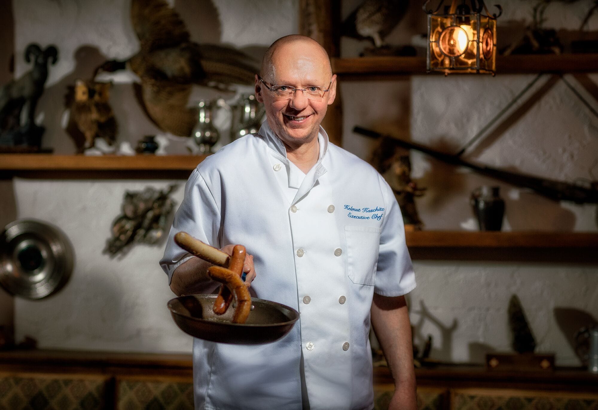 Ein Koch in weißer Uniform hält eine Pfanne mit Essen.