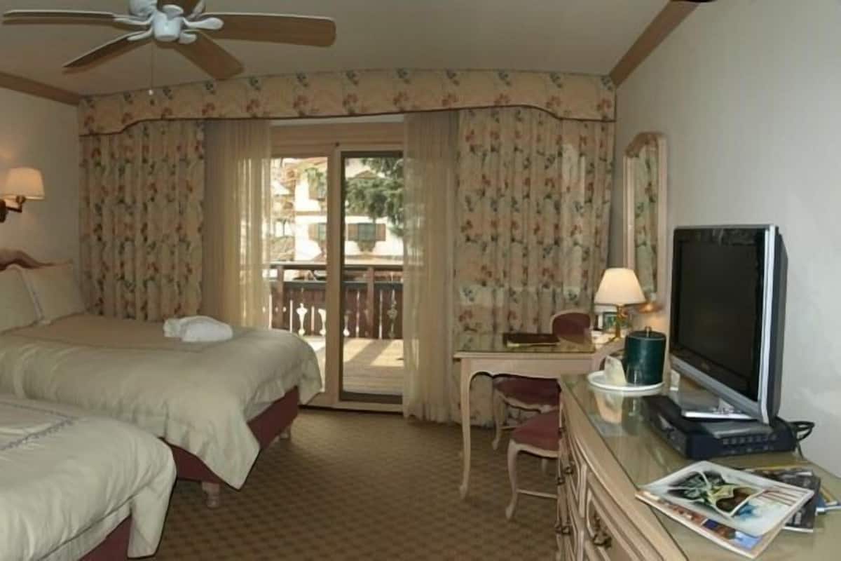 Een hotelkamer met twee bedden, een bureau met een computer, een televisie en een plafondventilator.