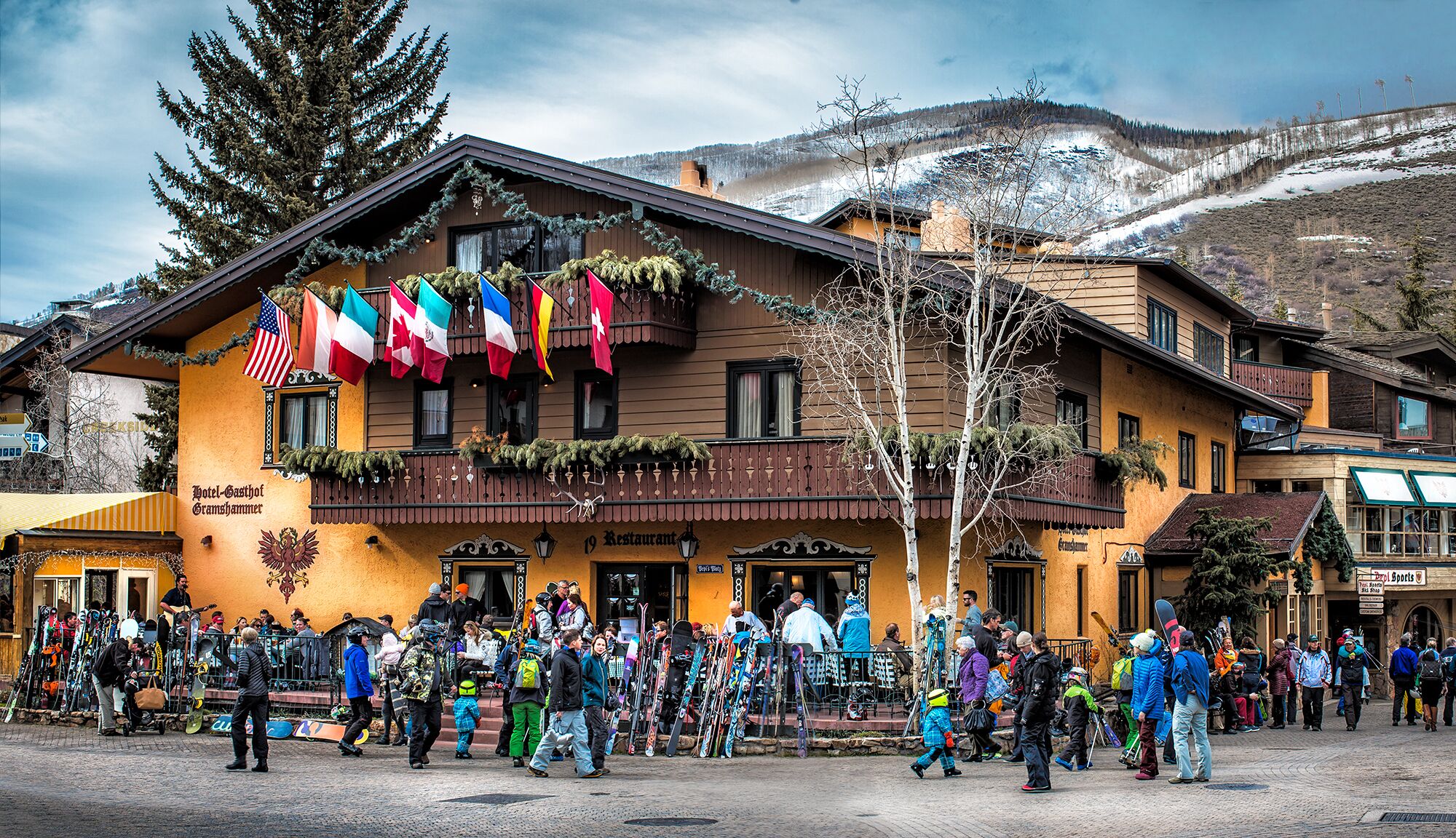 Un hôtel de style alpin traditionnel, doté d’un balcon orné de drapeaux et d’une enseigne indiquant qu’il s’agit d’un restaurant.