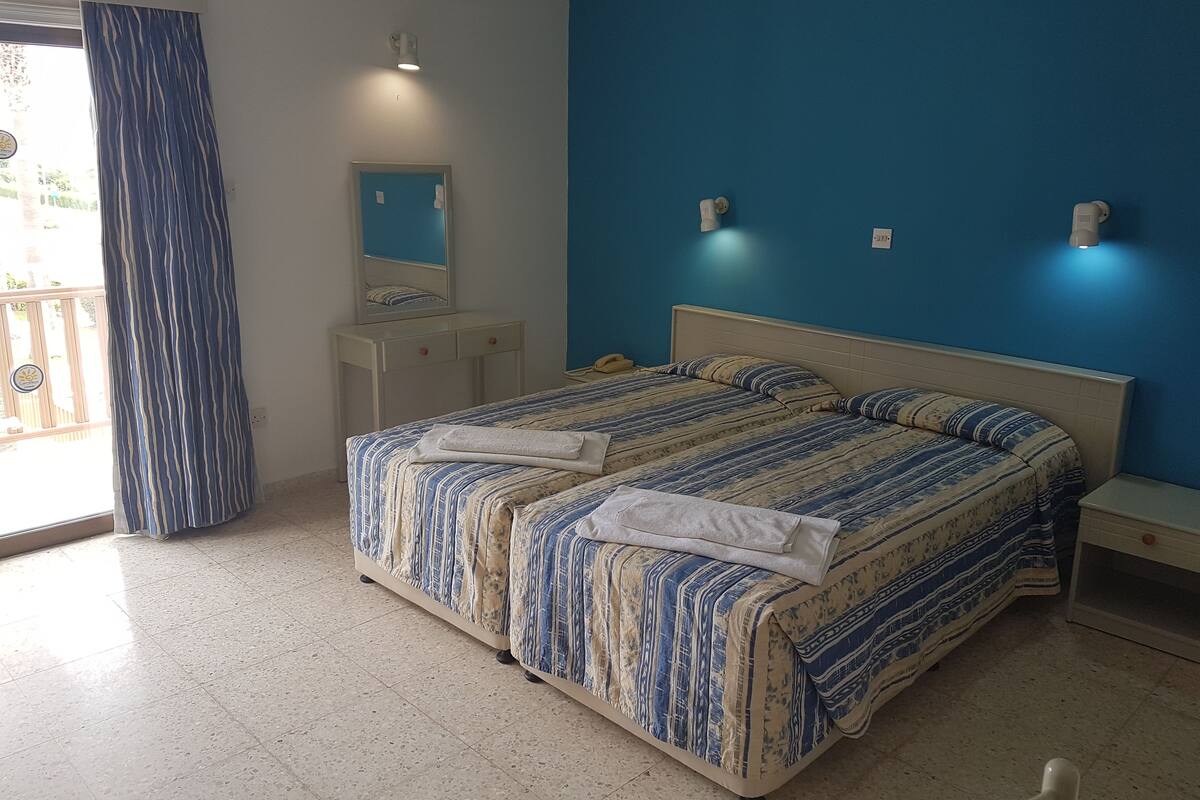 Una camera da letto con un letto grande, un comodino, un tavolino, una cassettiera, uno specchio e una finestra con tende.