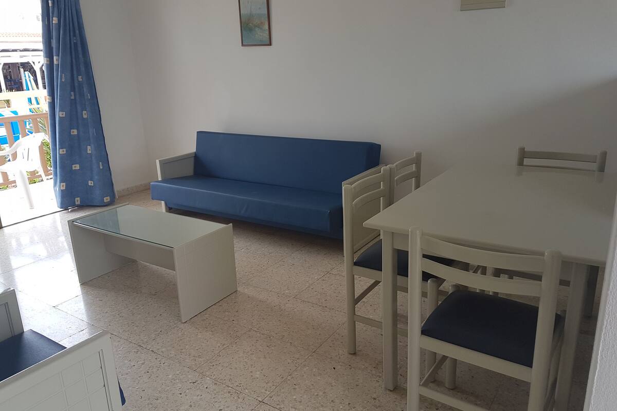 Una stanza piccola e luminosa con un divano blu, un tavolo bianco e due sedie.