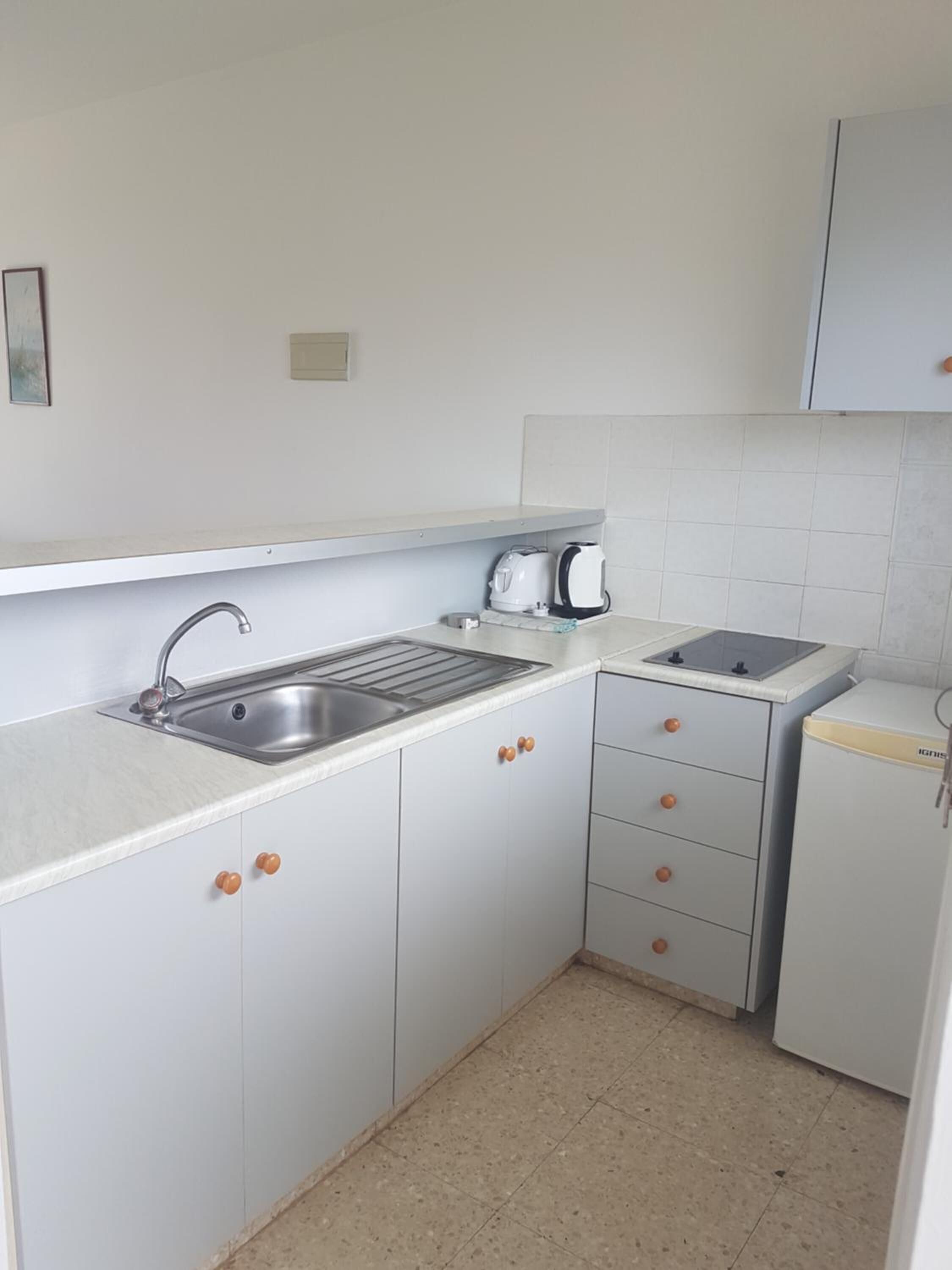 Una cocina compacta con un lavamanos, hervidor, tostadora y refrigerador.