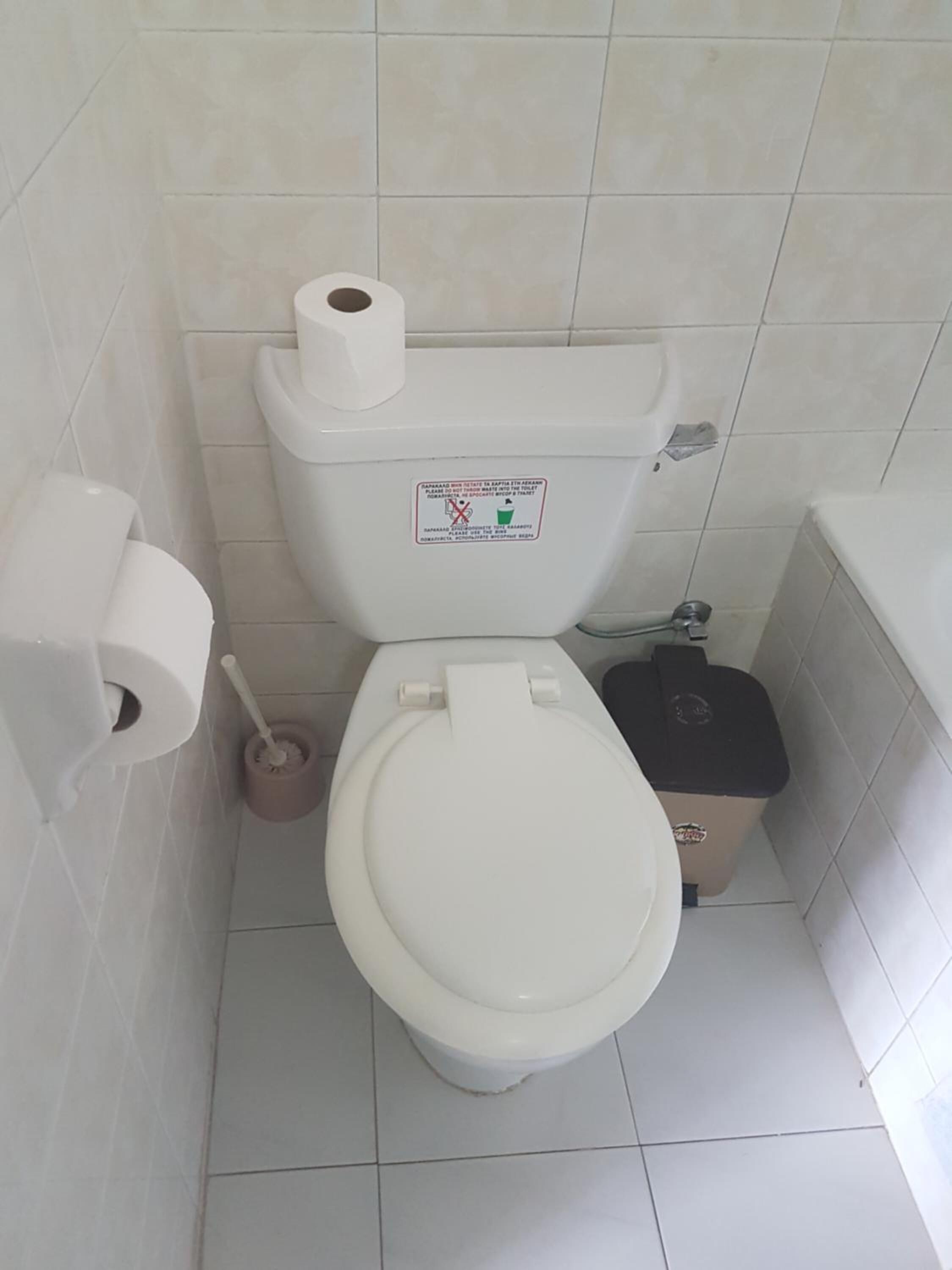 Ein kleines Badezimmer mit Fliesen, einer Toilette, einem Toilettenpapierhalter und einem Mülleimer.