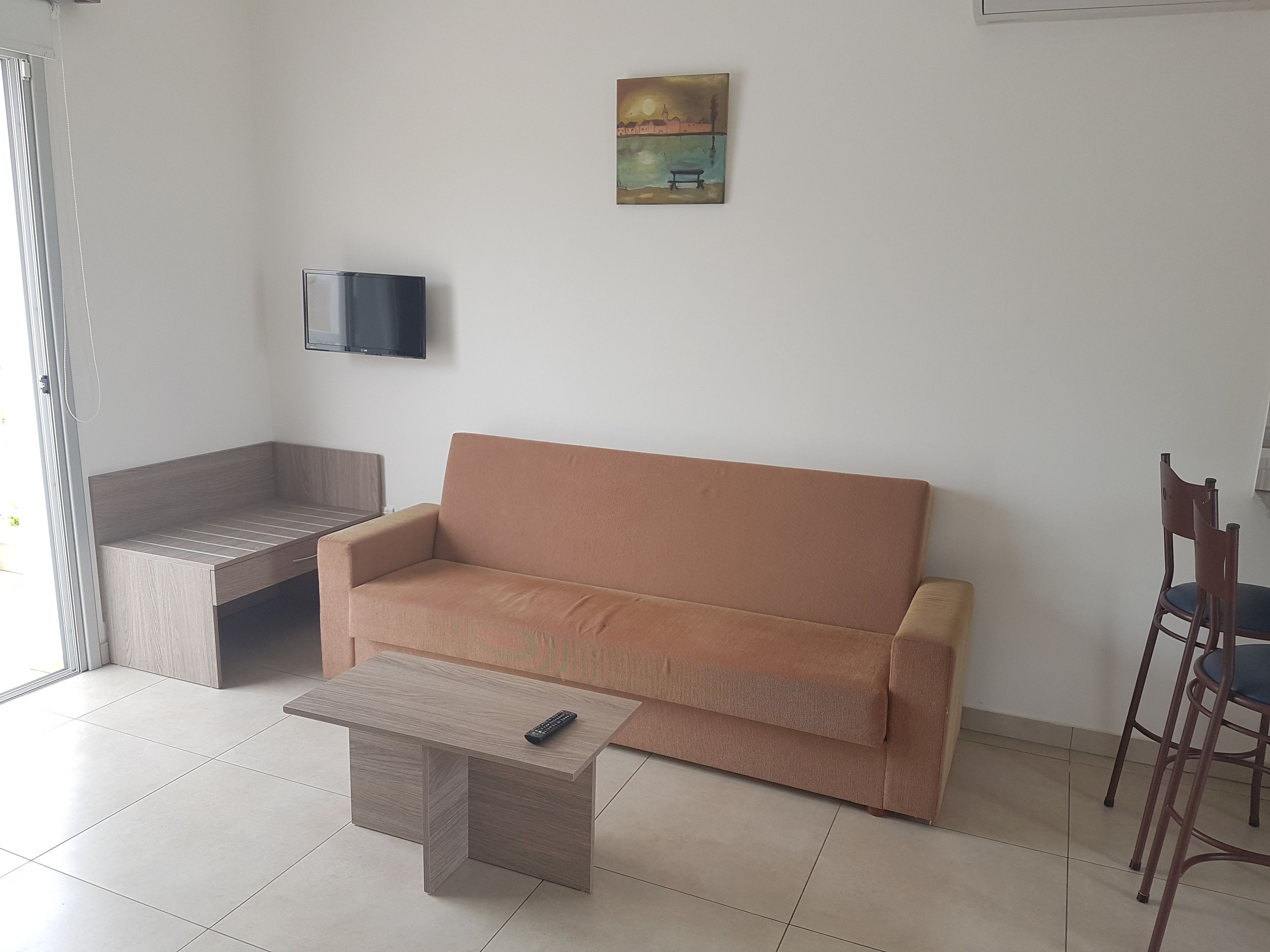 A living room with a sofa, a coffee table, a TV mounted on the wall, and a painting.