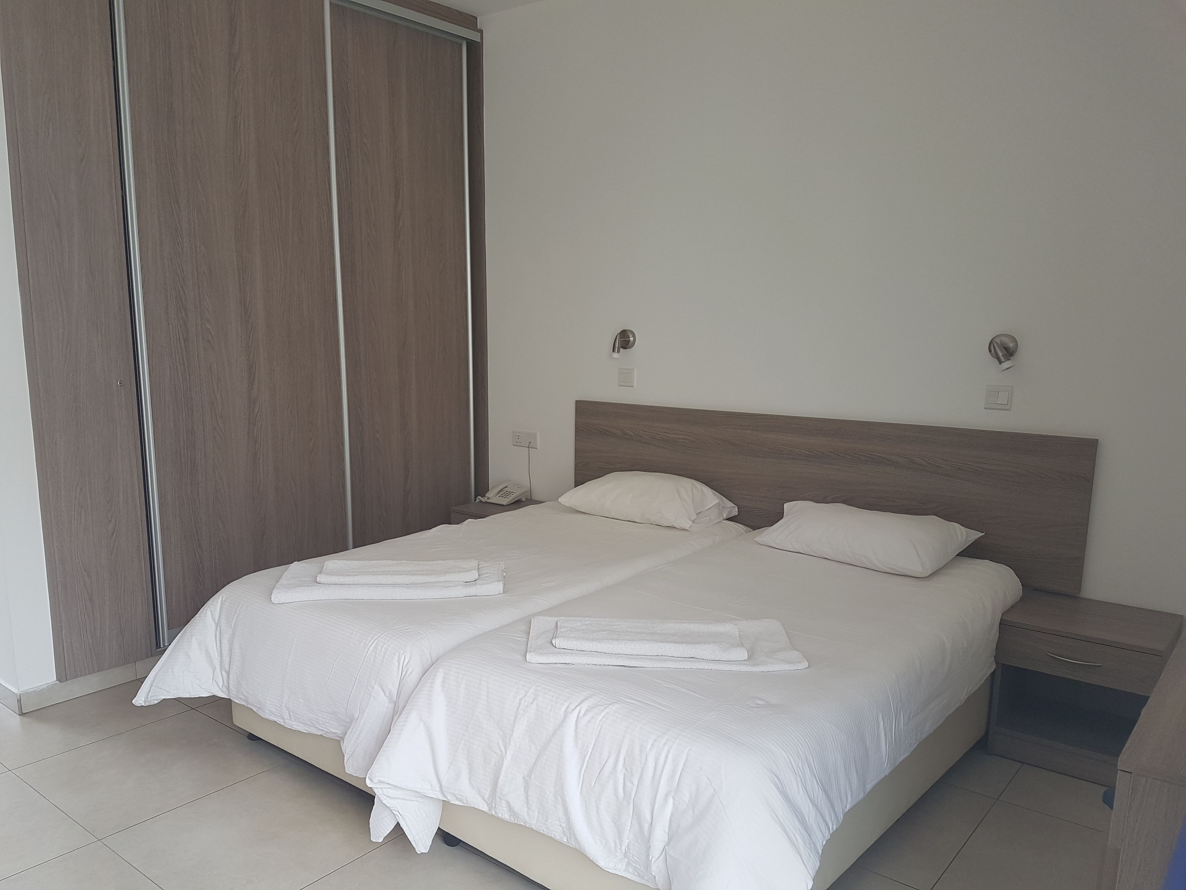 A neatly made double bed with white linens, a wooden headboard, and two bedside tables with lamps.