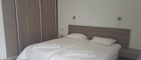 Un lit double bien fait, avec du linge de lit blanc, une tête de lit en bois et deux tables de chevet avec des lampes.