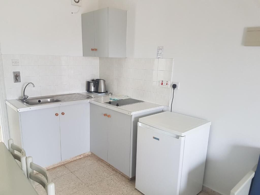 A compact kitchen with a sink, a small refrigerator, and a kettle.
