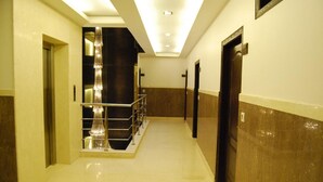 A hotel hallway with a marble floor, a staircase with a metal railing, and doors on both sides. - Walnut Castle (New Delhi)
