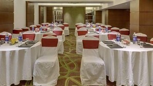 A conference room with round tables, each covered with white tablecloths and red chair covers. Tables are equipped with water bottles, notepads, and pens. The room has a carpeted floor and wooden paneling on the walls. - Walnut Castle (New Delhi)