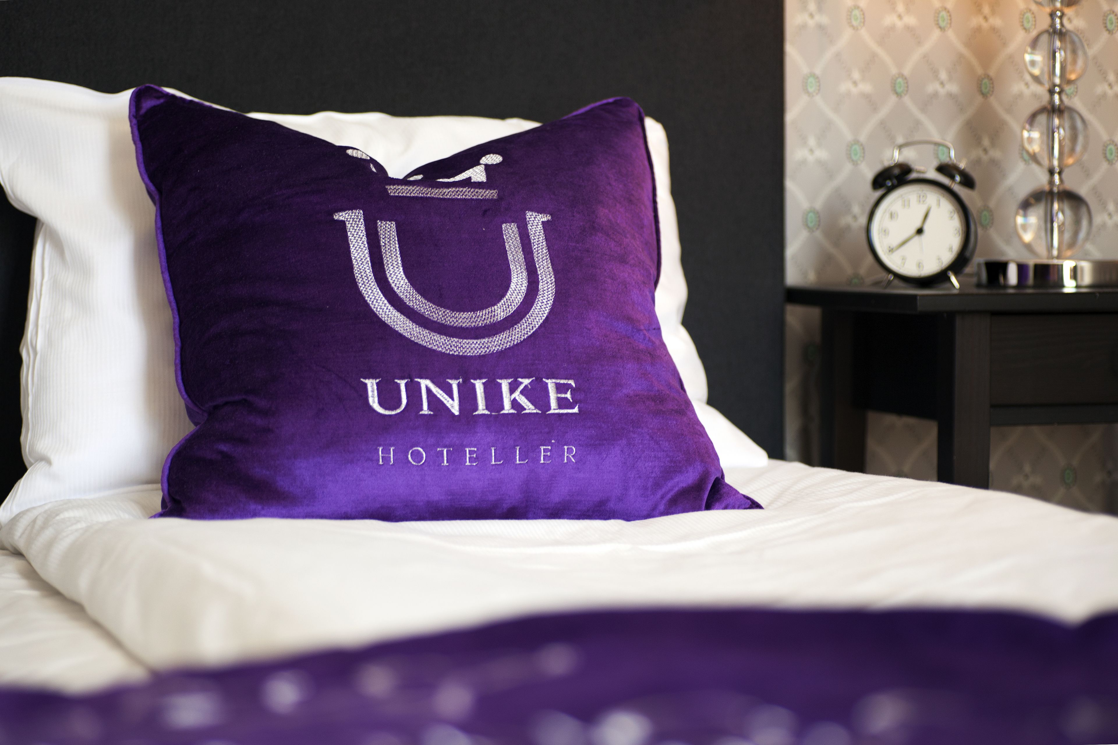 A bed with a purple pillow featuring the text "UNIKE HOTELLER".