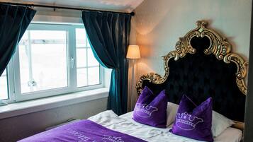 Une chambre d’hôtel avec un lit, un lustre, une fenêtre avec des rideaux et une lampe.