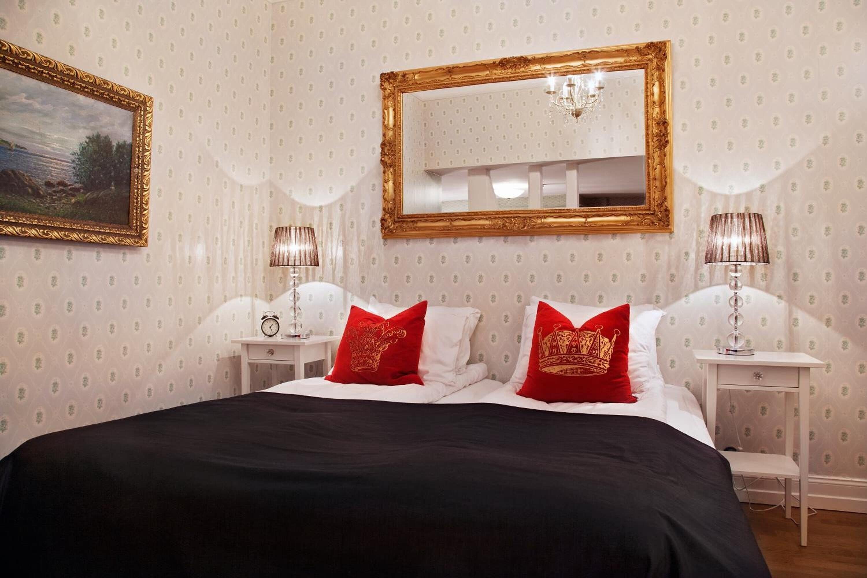 A neatly arranged bedroom with a large bed, two bedside tables, a mirror, and a painting on the wall.