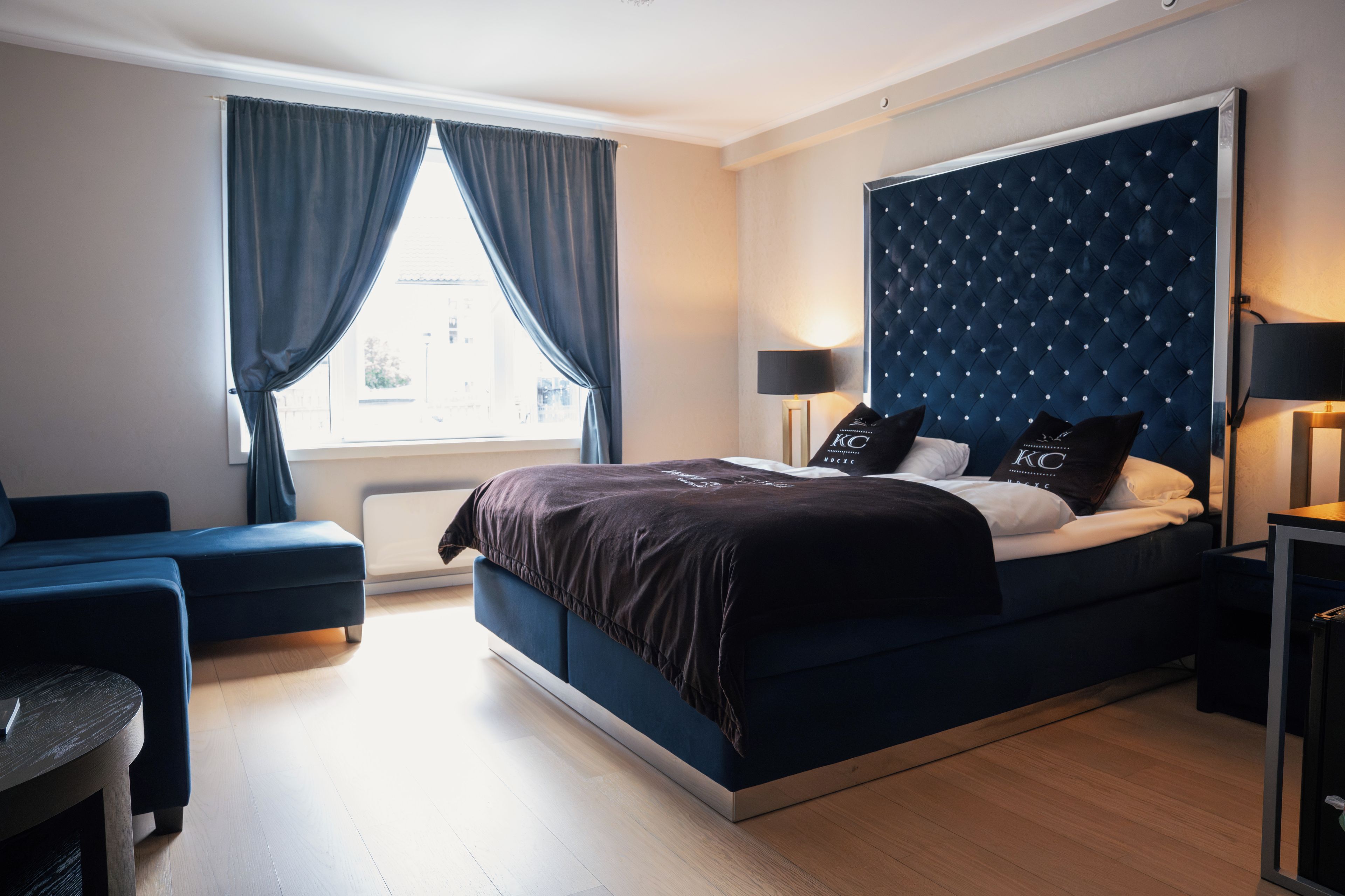 Un dormitorio moderno con una cama grande, una mesita de noche, una silla y una ventana con cortinas.
