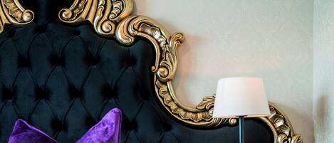 A bed with a black headboard, a purple pillow, a white pillow, and a black nightstand with a lamp.