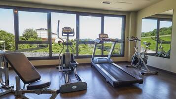 A gym with exercise equipment, large windows, and a view of greenery and buildings.