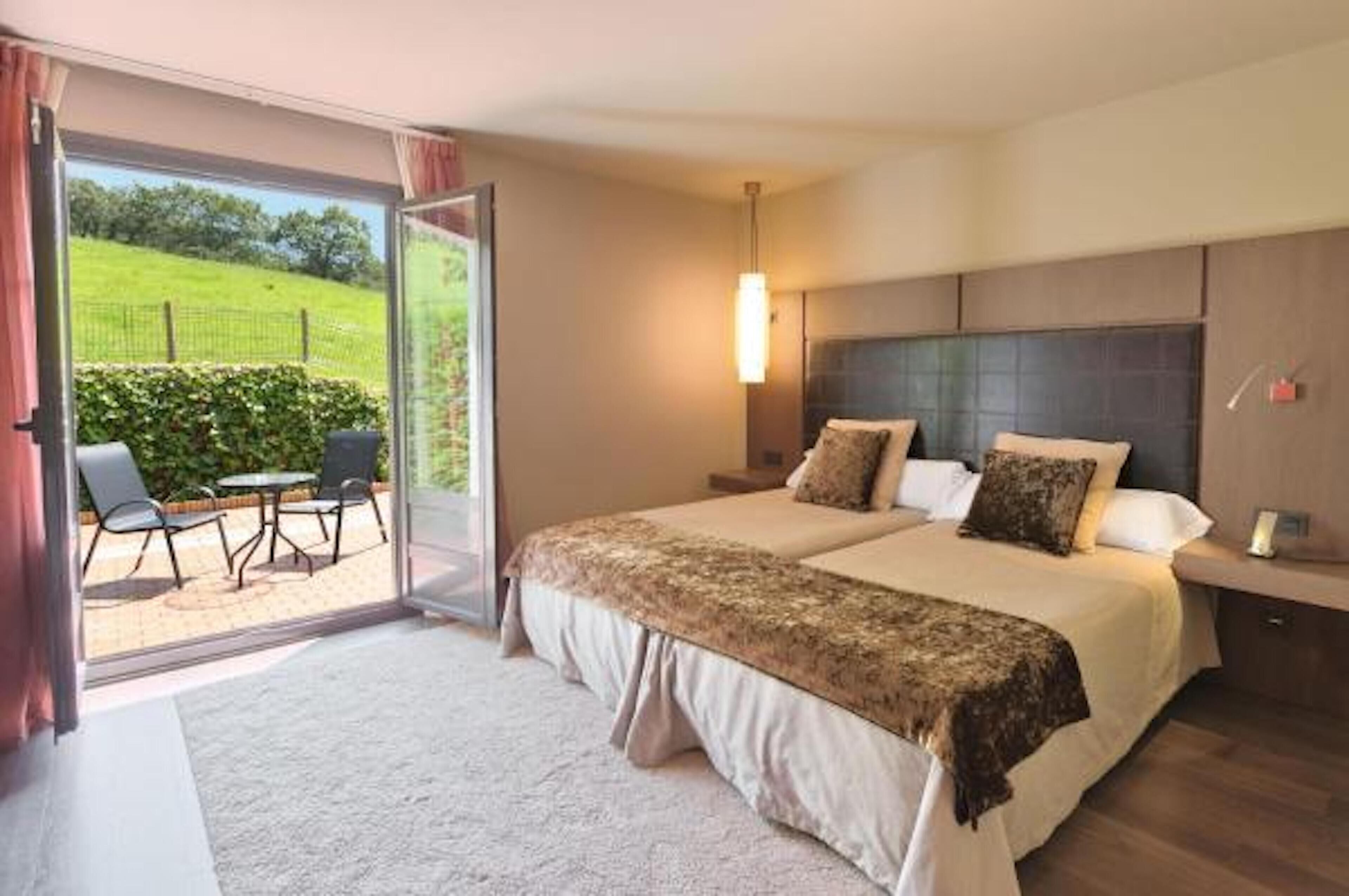 A double bed with a headboard, a bedside table, and a lamp. There is a sliding glass door leading to an outdoor seating area with a table and chairs.