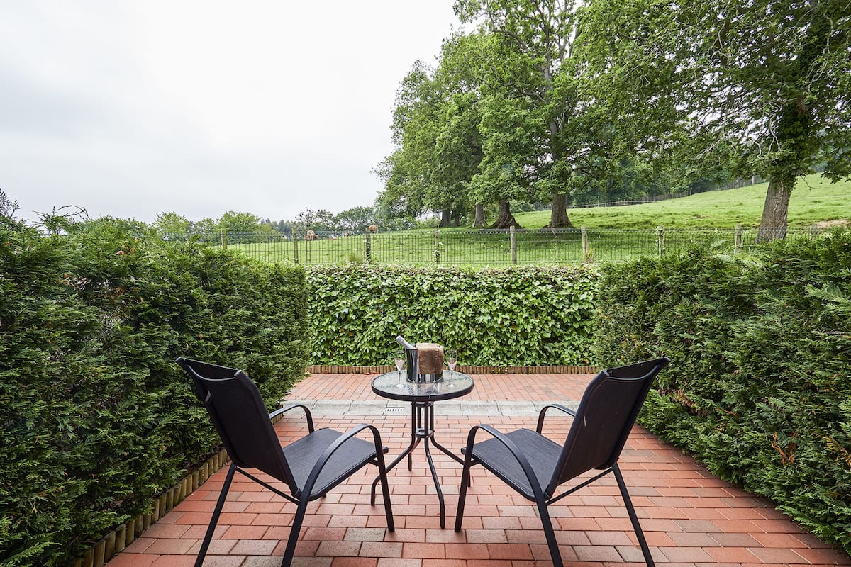 An outdoor patio with a brick floor, two black metal chairs, and a small round table with a glass and a bottle.