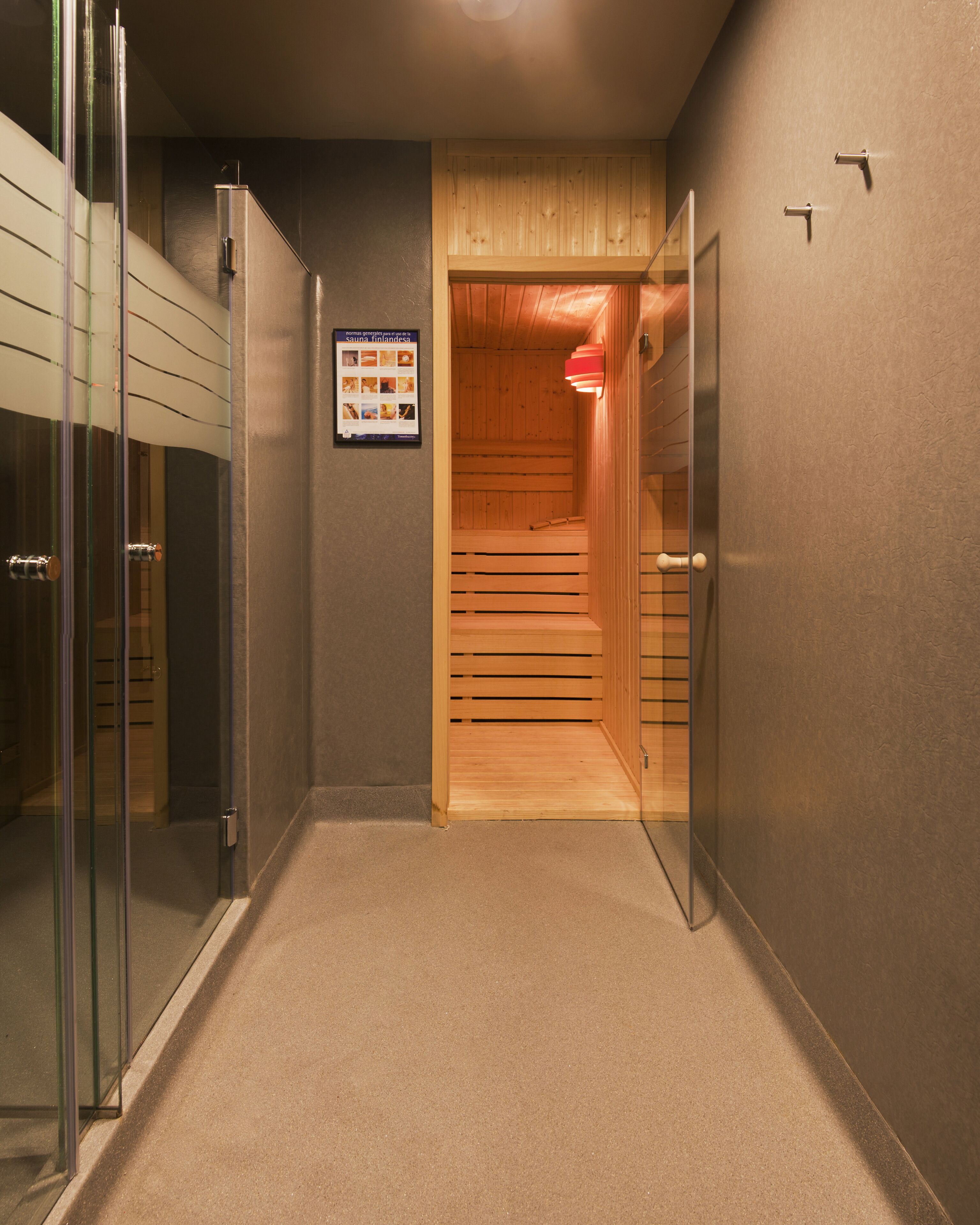 A hallway with a sauna room, a glass shower enclosure, and a wooden door.
