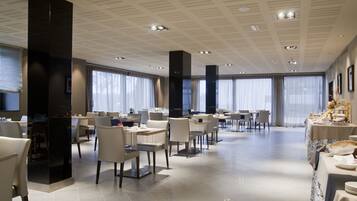 Un comedor amplio con varias mesas y sillas, ventanas grandes con cortinas translúcidas y un diseño de techo moderno.