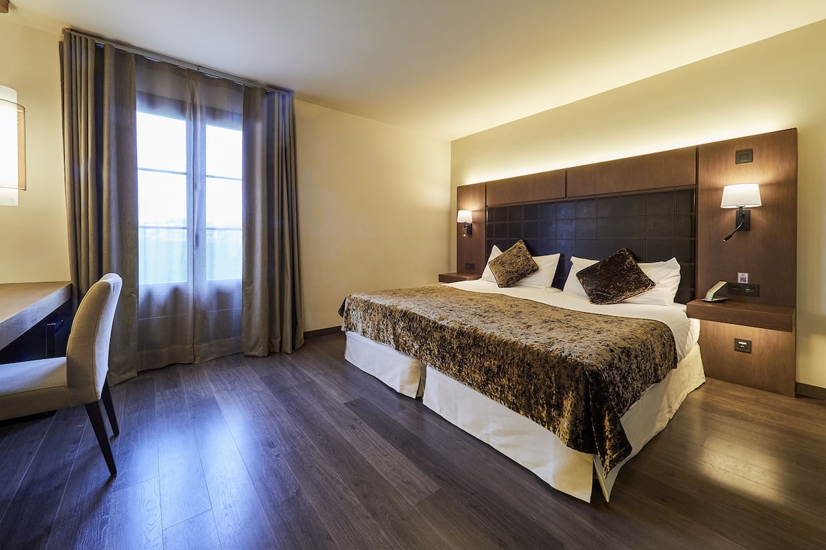 A hotel room with a bed, a desk, a chair, and a window with curtains.
