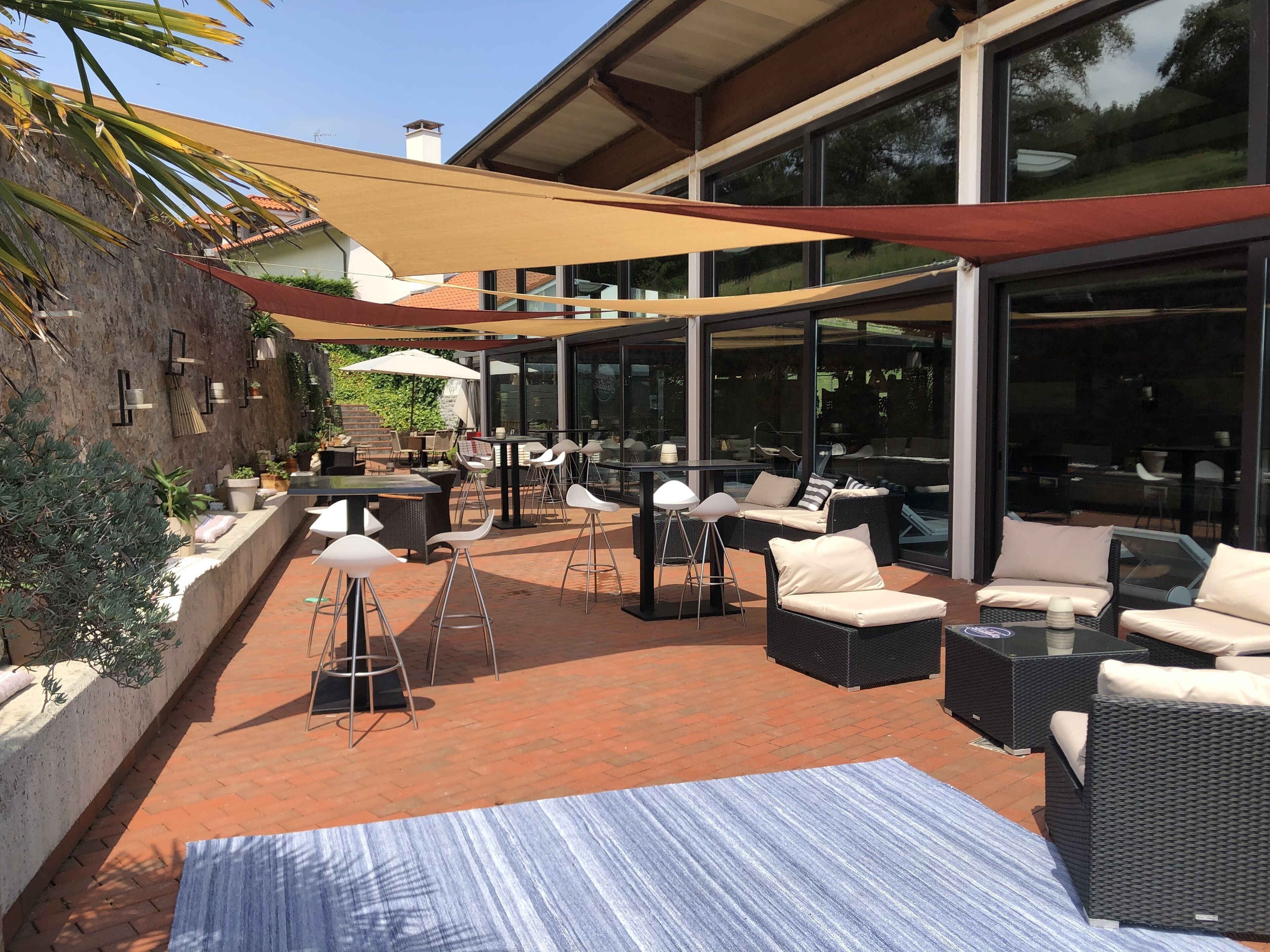 Une terrasse extérieure aménagée avec des meubles en osier, un tapis à rayures et un grand parasol offrant de l’ombre.